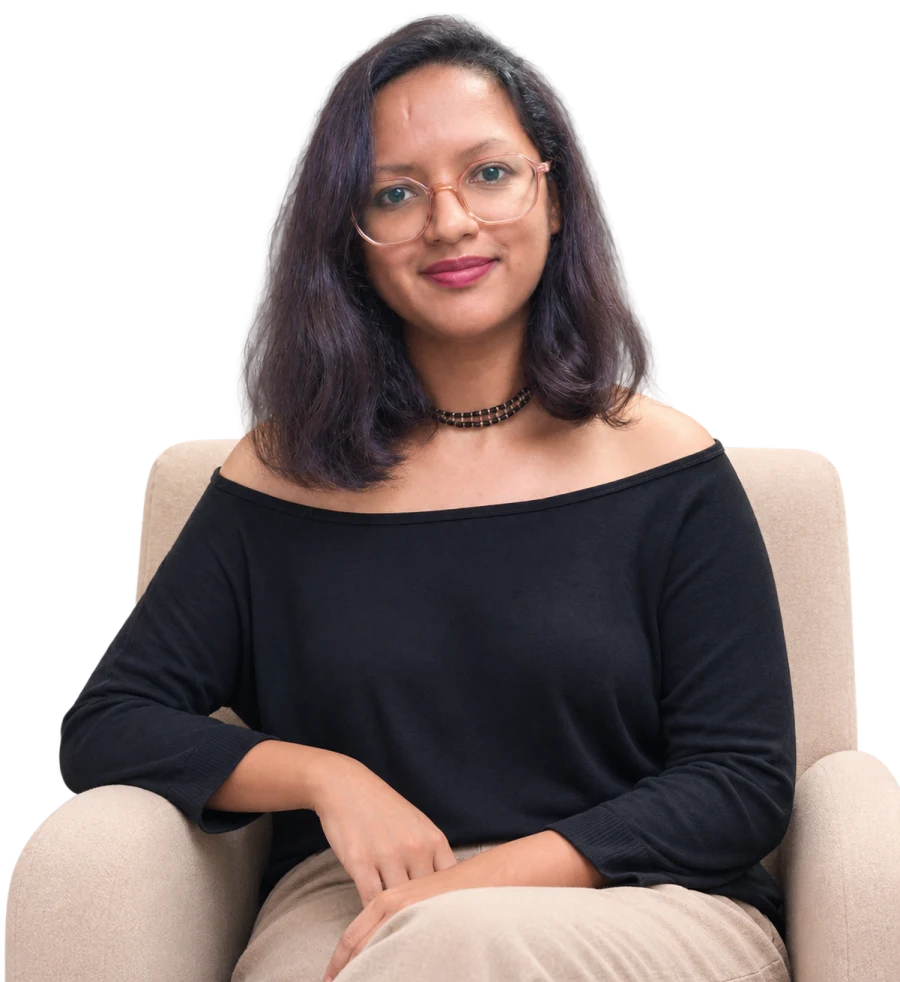 Harshita seated in an armchair, smiling, in a black top, cut out against the page background.